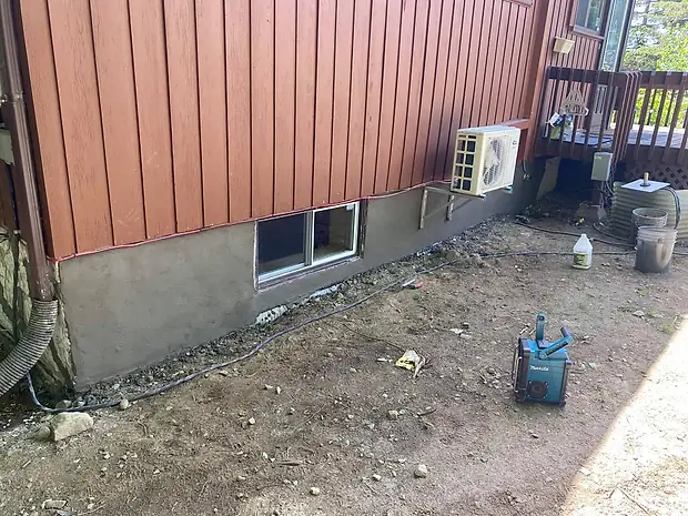 L'autre côté de la maison, déjà crépi d'un gris uniforme jusqu'au bas du mur, la fenêtre du sous-sol dégagée