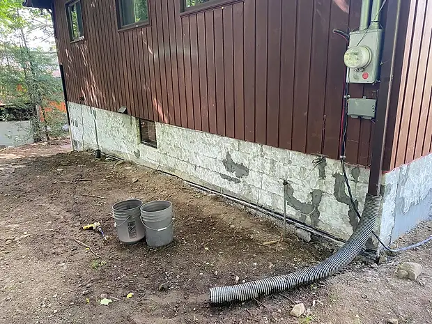 Un côté de la maison avant les travaux : le vieux crépi de la fondation se décolle par plaques, drain de plastique noir déroulé au sol