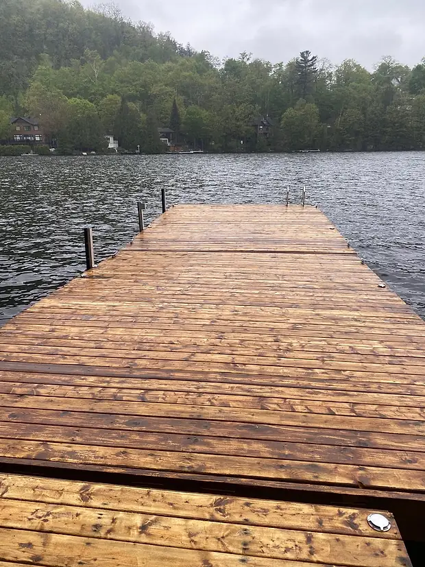 Le même quai mouillé sous la pluie, le bois encore doré avant la teinture, avançant sur le lac jusqu'aux poteaux