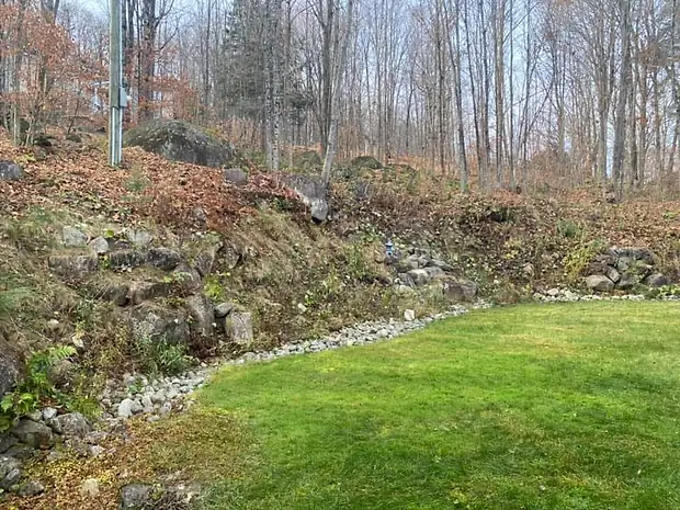La même pente dégagée, le muret de roches et la bande de galets le long de la pelouse