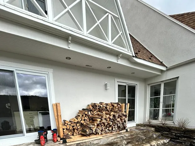 Le bois rangé dans son support contre le mur crépi blanc de la maison, sur la terrasse de pierre