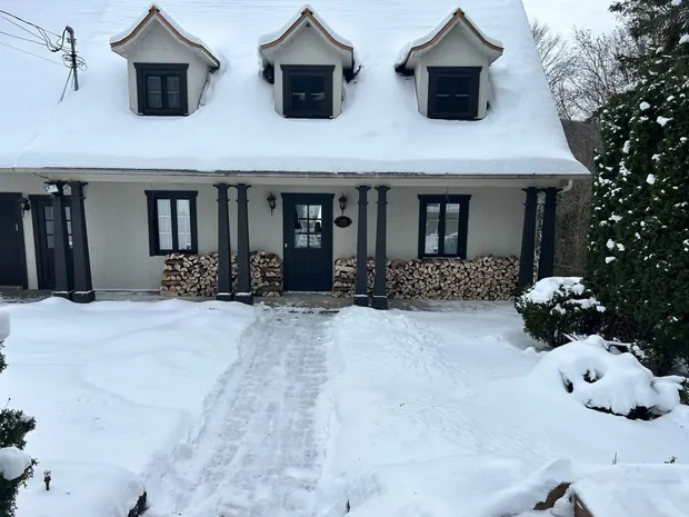 Façade de maison canadienne sous la neige, le bois cordé bien droit des deux côtés de la porte