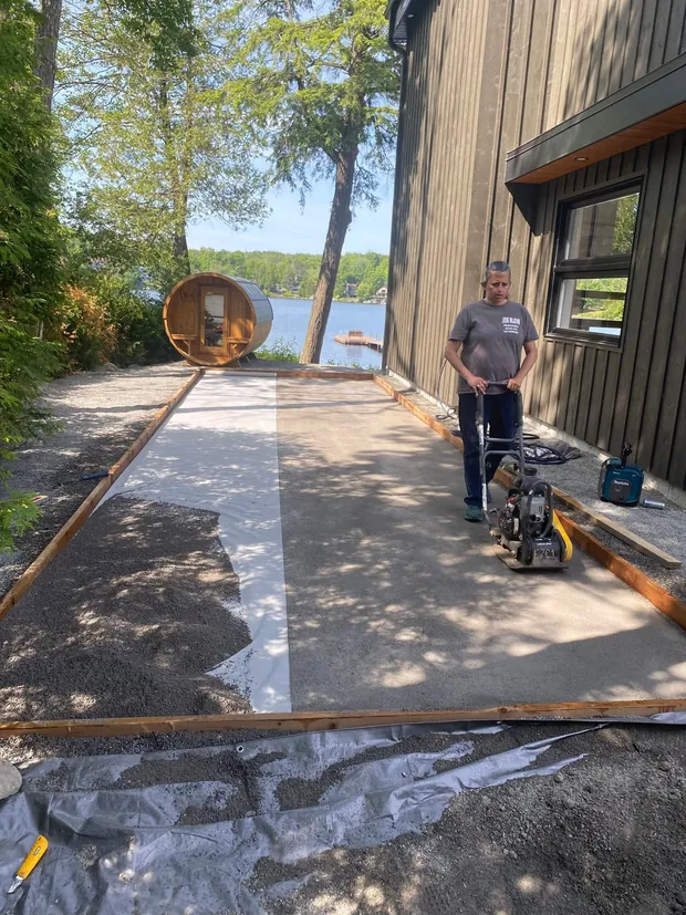Coffrage de bois, membrane et gravier compacté le long d'une résidence noire au bord d'un lac, avant la coulée