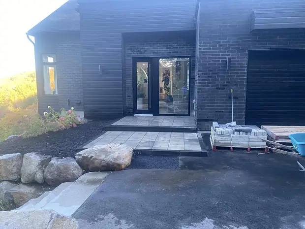 La même façade, l'entrée de dalles terminée jusqu'à la porte, blocs de roc et plate-bande