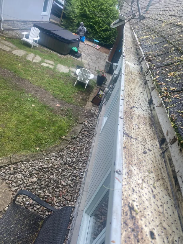 La même gouttière vidée, fond d'aluminium visible, même bande de gravier et même mur blanc