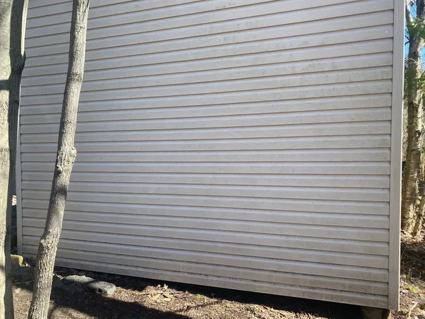 Mur de vinyle d'un cabanon, terni et sale, en plein soleil de côté
