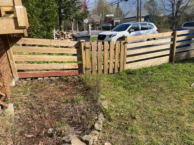 Clôture de bois brut sur un terrain de coin, planches horizontales et barrière à barreaux, au printemps