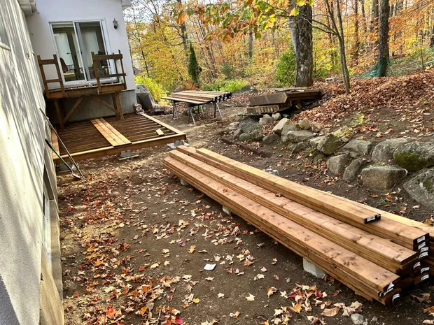 Le patio en construction : les premières planches neuves posées sur la structure, les madriers empilés au sol et la table de sciage montée