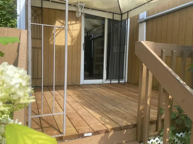 Le patio refait en bois neuf jusqu'à la porte-patio, sous la toile du gazebo, la rampe brune à droite
