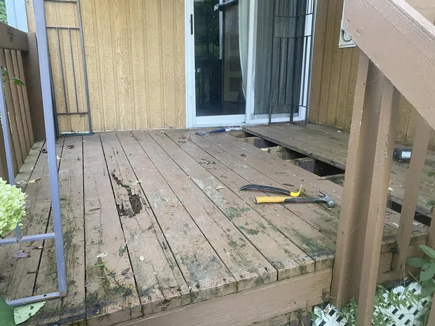 Vieux patio de bois brun devant une porte-patio, planches pourries et trouées, marteau et pied-de-biche posés dessus