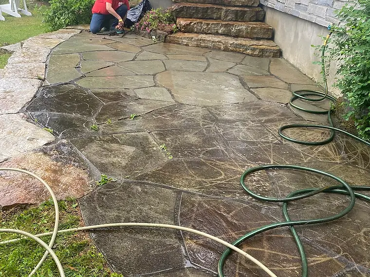 Terrasse de pierre plate lavée à l'eau, les joints en train d'être refaits, deux boyaux d'arrosage déroulés au sol
