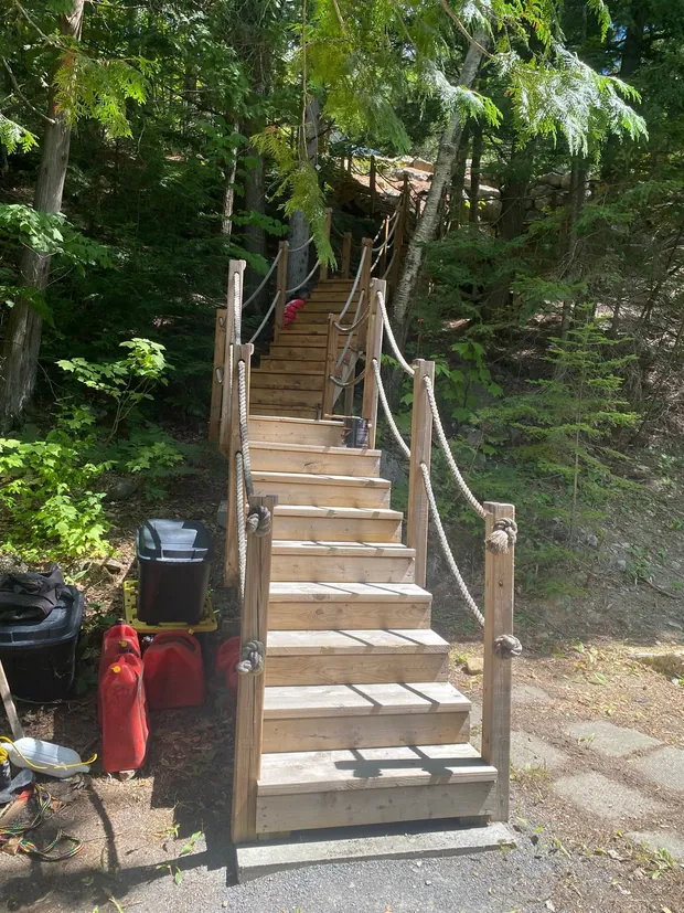 Long escalier de bois neuf à flanc de pente, encore sans teinture, avec des rampes en corde de chanvre
