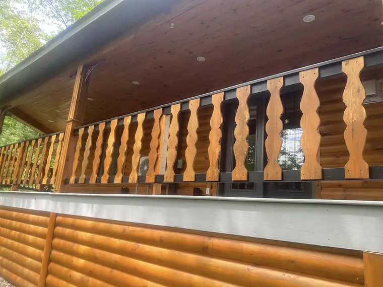 Gros plan d'une galerie : barreaux de bois découpés en vagues, fraîchement teints, billots dorés, plafond de bois