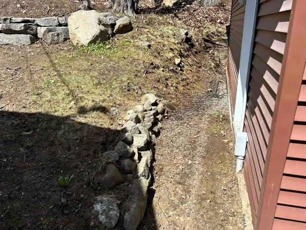 Le pied du même bâtiment entièrement dégagé, la bordure de roches et la terre nue redevenues visibles